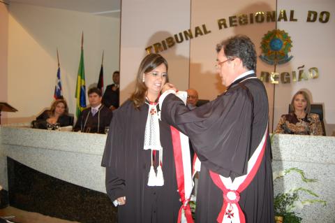 homem de toga em pé entregando uma faixa a uma mulher de toga em pé