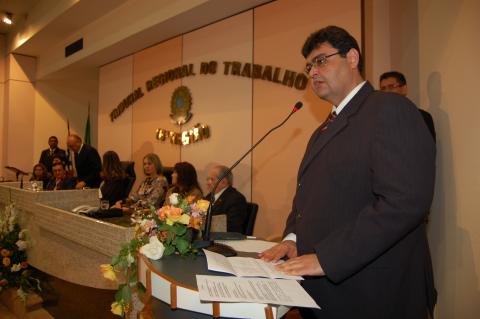 Homem de terno, em pé, em frente a um tribuna discursando
