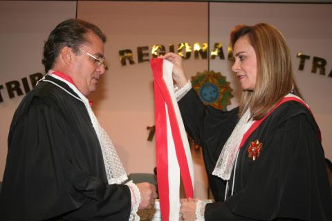 homem de toga em pé recebendo uma faixa de uma mulher de toga em pé