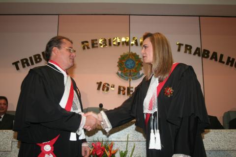 homem de toga cumprimentando uma mulher de toga, ambos em pé.