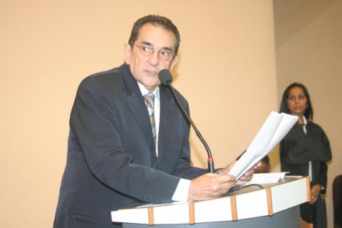 Homem de terno, em pé, em frente a um tribuna discursando