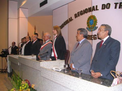 pessoas em frente a uma mesa de honra, em pé, com várias autoridades