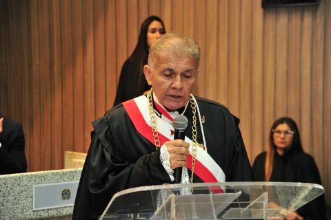 Homem de toga, em pé, em frente a um tribuna discursando