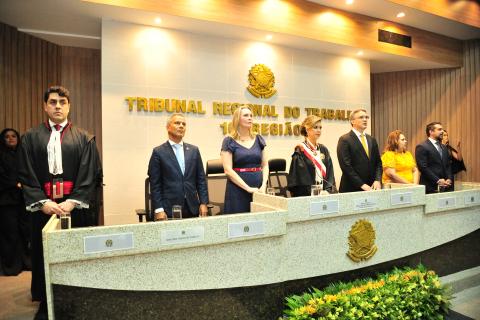 pessoas em frente a uma mesa de honra, em pé, com várias autoridades