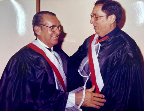 dois homens de toga em pé, cumprimentando-se e pousando para foto.