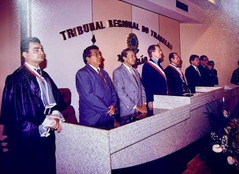 pessoas em frente a uma mesa de honra,em pé posicionadas para execução do Hino Nacional