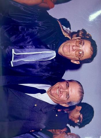 Dois homens um de terno e outro de toga preta, todos em pé, pousando para foto